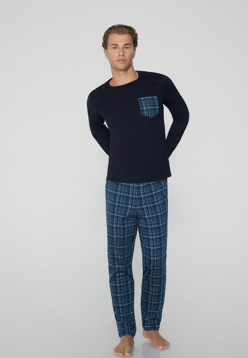 Parte superior de pijama de manga larga en color navy con un bolsillo a cuadros, combinada con pantalones de cuadros azules. El material parece suave, adecuado para ropa de dormir.
