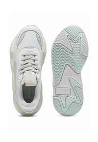 Bílé a světlé šedé tenisky Puma zobrazené z pohledu shora a ze spodní části, s krajkami a texturovanou gumovou podrážkou s logem "Running System".