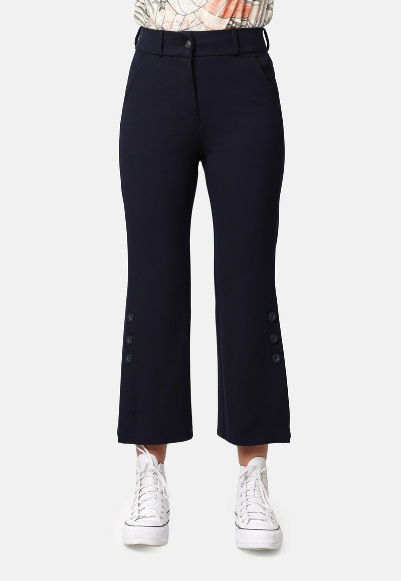 Pantalones cortos de color azul marino, confeccionados en una tela suave, con un detalle lateral abotonado, bolsillos delanteros y una cinturilla ajustada. Combinados con zapatillas blancas.
