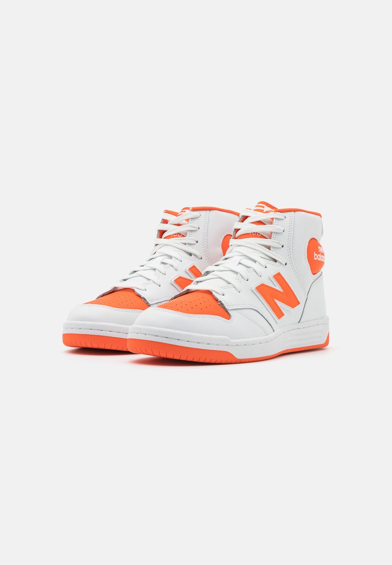 Zapatillas altas en blanco y naranja vibrante. Cuentan con puntera perforada, paneles texturizados y un acento de logo en el lateral. Suela de goma.