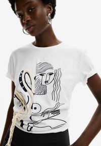 Camiseta blanca de algodón con dibujos en línea negra de figuras abstractas y animales, con un detalle de cuerda texturizada en la parte frontal.