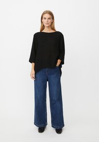 Schwarzes, übergroßes Strickoberteil mit weitem Ausschnitt, kombiniert mit hoch taillierter, locker sitzender dunkelblauer Jeans und schwarzen Stiefeletten.