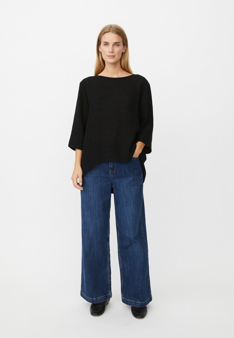 Schwarzes, übergroßes Strickoberteil mit weitem Ausschnitt, kombiniert mit hoch taillierter, locker sitzender dunkelblauer Jeans und schwarzen Stiefeletten.