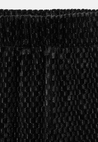 Čierna textúrovaná tkanina s vystúpeným vzorom a jemným leskom, s elastickým pásom na vrchu.