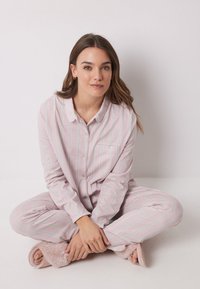 Pigiama a righe rosa con linee verdi e bianche; tessuto morbido, camicia con bottoni e tasca, e pantaloni abbinati. Include pantofole rosa morbide.