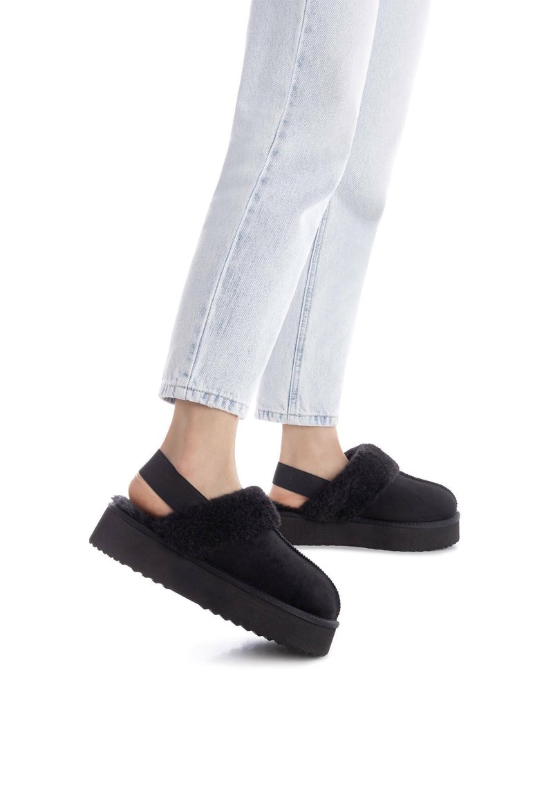 Sorte platform sko lavet af ruskind og pels, med en polstret bånd over toppen og elastisk strop bagpå, båret med lyse jeans.