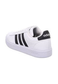 Weißer Adidas Low-Top-Sneaker mit schwarzen Streifen und Fersenlasche, sichtbares Adidas-Logo auf Ferse und Sohle, Seitenansicht.