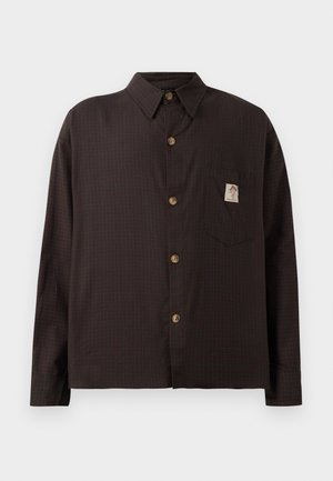 Cămașă în carouri maronii cu guler ascuțit, nasturi pe față, un buzunar pe piept cu un patch cu logo și mâneci lungi.