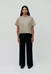 Tricou scurt de culoare verde măsliniu, cu mâneci largi, asortat cu pantaloni negri cu talie înaltă și croială largă. Modelul stă pe un fundal neutru.