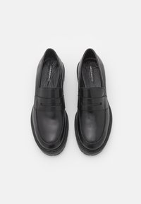 Sapata loafers pretas de couro com uma textura suave, bico arredondado e uma faixa decorativa na parte superior. Apresenta uma sola costurada.