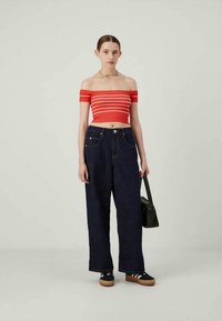 Κόκκινο και άσπρο ριγέ crop top με έξω τους ώμους, ψηλόμεσο σκούρο μπλε τζιν με φαρδιά μπατζάκια, μαύρη τσάντα και μαύρα παπούτσια με άσπρες ρίγες.