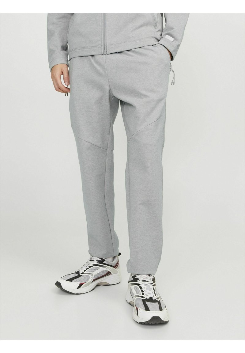 Joggers deportivos grises hechos de una tela suave, con un corte ajustado, bolsillos laterales y detalles en panel. Combinados con zapatillas voluminosas en blanco y negro.