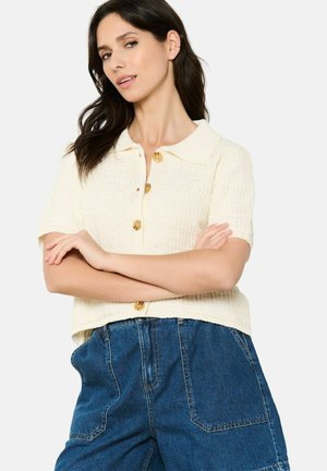 Short-sleeve cream knit top with a collared neckline and three-button front closure, paired with high-waisted denim shorts.