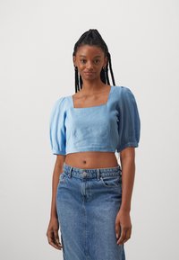 Haut court bleu clair avec un décolleté carré et des manches bouffantes, associé à une jupe en denim taille haute. Texture lisse, design décontracté.