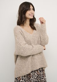 Beige gebreide sweater met een V-hals, een textuurpatroon en een ontspannen pasvorm, gecombineerd met een jurk met een patroon van luipaardprint.