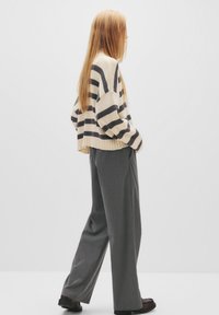Strikket, lys beige og marineblå stribet sweater med dropped shoulders og ribbet kant, parret med løstsiddende grå bukser og mørke sko.