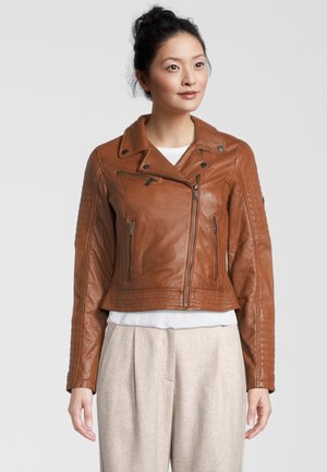 Braune Leder-Motorradjacke mit asymmetrischem Reißverschluss, tailliertem Design und geripptem Muster an den Ärmeln. Trägt man über einem weißen Oberteil.