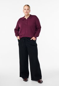 Camisa polo de manga larga burdeos con cuello y tapeta de botones, combinada con pantalones negros sueltos y zapatos negros brillantes. Fondo liso.