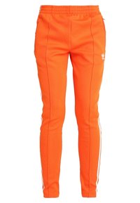 Oranssi Adidas-housut, joissa on valkoiset sivuosat ja elastinen vyötärö, kireä malli.