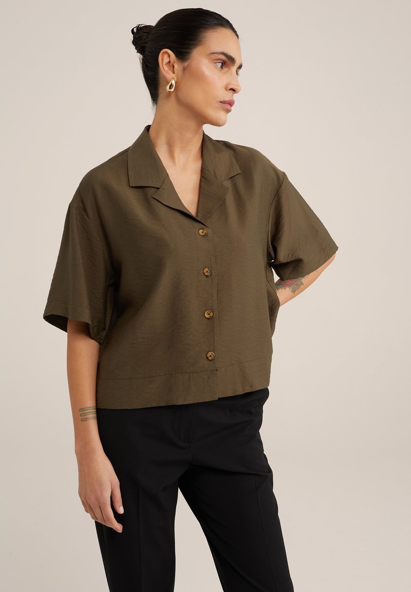 Camicia a maniche corte verde oliva in tessuto leggero, con vestibilità rilassata, colletto a scollo a V e chiusura frontale con bottoni in legno.