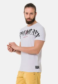 Weißes Baumwoll-T-Shirt mit kräftigem schwarzem Grafiktext und roten Akzenten, mit Rundhalsausschnitt und kurzen Ärmeln; Etikett am Saum.