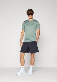 Miętowozielona koszulka sportowa z krótkim rękawem oraz granatowe szorty, z logo Nike. Model nosi ciemne okulary przeciwsłoneczne oraz białe buty sportowe z białymi skarpetkami.
