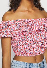 Off-shoulder bloemen crop top met een roze achtergrond en oranje en paarse bloemen, met volantranden bij de mouwen en een gathered taille.