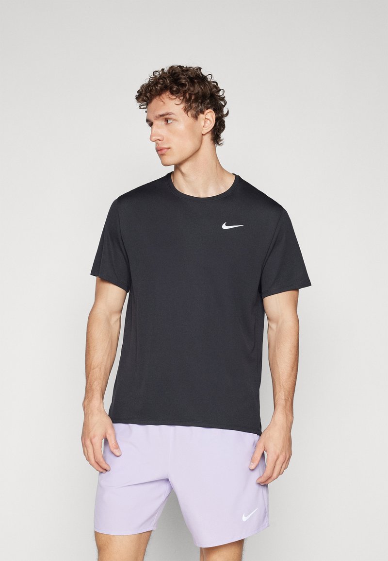 Nike musta musta t-paita lyhythihaisella ja pyöreällä kauluksella, jossa on pieni valkoinen logo rinnassa. Yhdistetty vaaleanliiloihin shortsit.