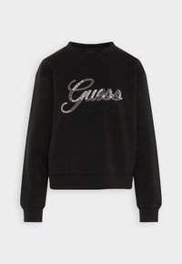 Svart sweatshirt med rundad halsringning, med en glänsande strassprydd "Guess"-logotyp och texten "EST. 1981" över framsidan.