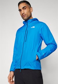 Sinine veekindel jakk kapuutsi ja tõmblukuga rinnataskuga, reguleeritavad mansetid. Esiküljel on The North Face logo vasakul küljel.