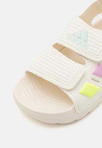 Hvit sandal med teksturerte stropper; har borrelås-lukking, fargerike aksenter i gul, rosa og aqua, samt en teksturert gummisåle.