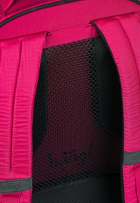 Zaino pink con tessuto testurizzato, spallacci imbottiti e pannello in rete nera. Presenta un logo sulla tracolla e cuciture rinforzate.