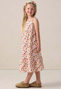 Blumenkleid mit einem hellpfirsichfarbenen Hintergrund, rosa und roten Kirschmustern, dünnen Trägern und einem gestuften Saum. Begleitet von hellbraunen Slippers.