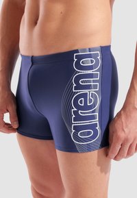 Marinefarbene Badeshorts aus dehnbarem Material mit einem weißen "arena"-Logo und einem gebogenen Liniendesign entlang der Seite. Enganliegender Schnitt.