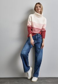 Maglione a maglia grossa color crema con righe orizzontali rosa e rosse, abbinato a jeans denim larghi e sneakers bianche.