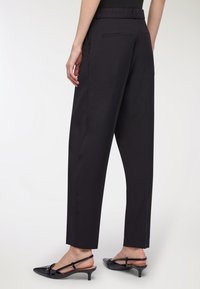 Czarne spodnie fasonu klasycznego z prostą nogawką, o gładkiej fakturze, z tylnymi kieszeniami i paskiem w talii. W zestawie z czarnymi butami na obcasie typu slingback.