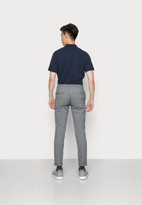 Marineblå kortærmet polo t-shirt parret med grå tapered bukser, der har opkrøllede manchetter og elastisk talje, suppleret med grå sneakers.