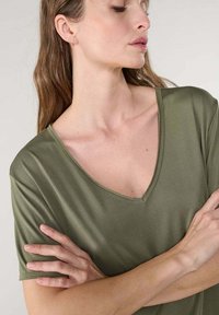 Camiseta de manga corta en verde oliva con un escote en V profundo, hecha de material suave, con un ajuste relajado y detalles de costura mínimos.