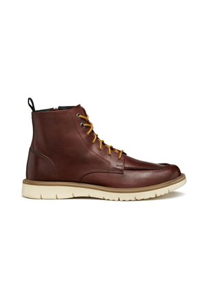 Brown leather ankle boot with yellow laces, rounded toe, beige rubber sole, and a black pull tab at the back. Smooth texture with minimal detailing.