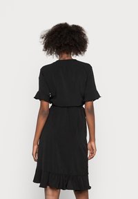 Vestido negro con mangas cortas y volantes, cintura con cinturón y dobladillo de volantes en capas. Textura suave, diseño a la altura de la rodilla.