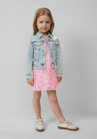 Veste en denim, bleu clair, avec deux poches poitrine ; robe plissée rose avec motifs colorés ; baskets beige avec semelles marron.