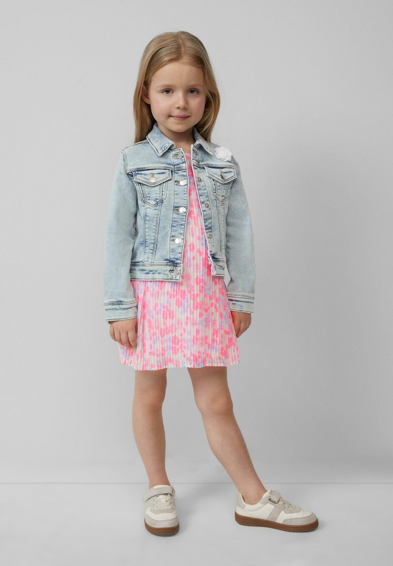 Veste en denim, bleu clair, avec deux poches poitrine ; robe plissée rose avec motifs colorés ; baskets beige avec semelles marron.