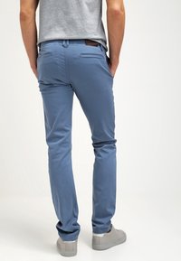 Ljusblå chinos i bomull, med slim fit, bakfickor och en brun läderlapp i midjan. Bärs med grå sneakers.