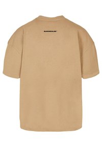 Ylihinnoiteltu beige t-paita, joka on valmistettu puuvillasta, ja siinä on lyhyet hihat, pyöreä kaula-aukko sekä musta logo painettuna selkäpuolella kaula-aukkoa lähellä.