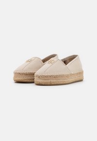 Espadrilles en toile beige avec des semelles en jute tressé, dotées d'un bout arrondi et d'un logo décoratif doré à l'avant.