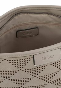 Beige synthetische Handtasche mit durchbrochenem Design. Das Innere verfügt über eine Reißverschlusstasche und ein Markenlabel. Glatte Textur mit Nahtakzenten.
