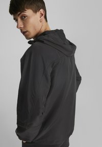 Svart hettejakke laget av glatt, lett stoff; har sømmer og en avslappet passform; vist fra baksiden med en lett vridd profil.