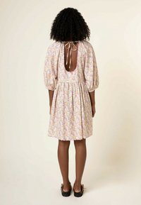 Robe d'été fleurie avec un dos décolleté, des manches ballon et une jupe froncée. Principalement rose pastel, avec des touches de fleurs jaunes, bleues et vertes.