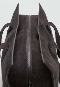 Bolso de ante marrón oscuro con cierre de cremallera, dos asas y ribete liso. Los lados del bolso están abiertos, mostrando un diseño minimalista.