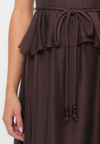 Bordeauxrotes Kleid mit gerafftem Bund und Bindegürtel, verziert mit Perlenakzenten. Weicher, strukturierter Stoff mit fließender Silhouette.